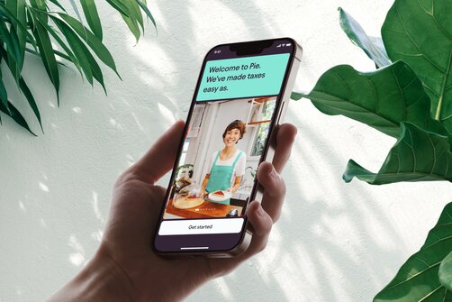 Hand holding smartphone showing app with leafy background.