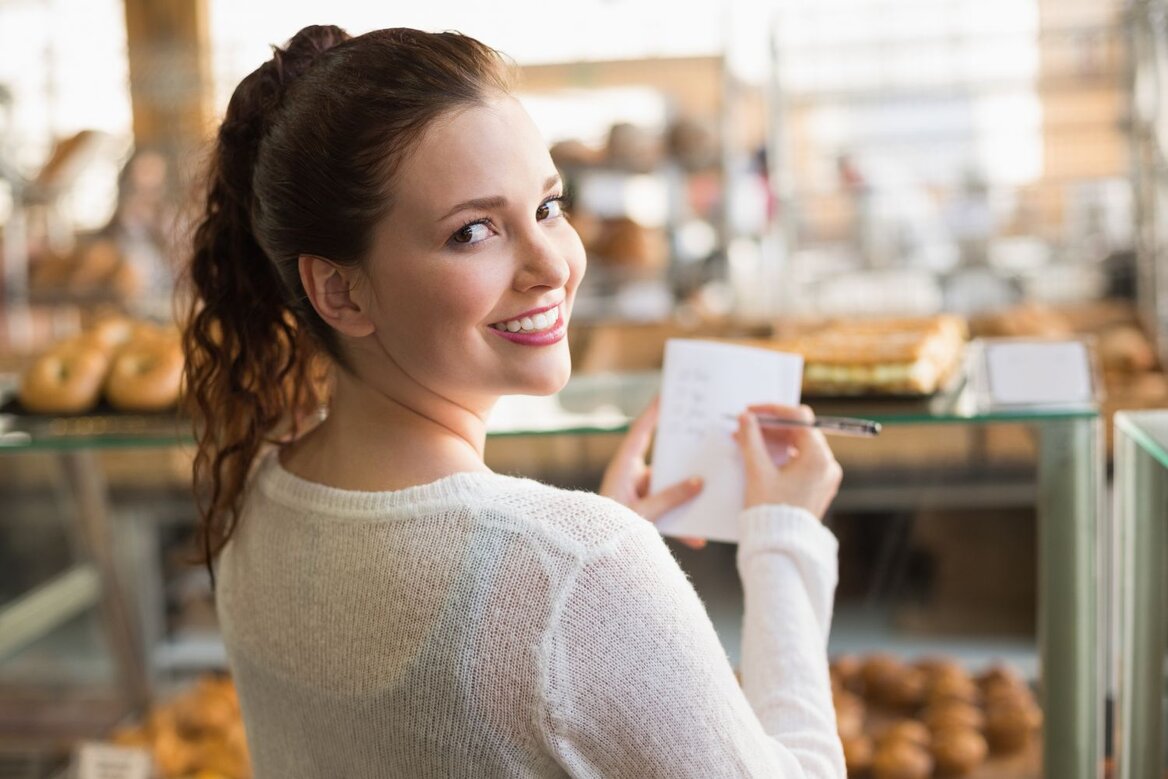 Smiling woman writing notes inside busy bakery shop