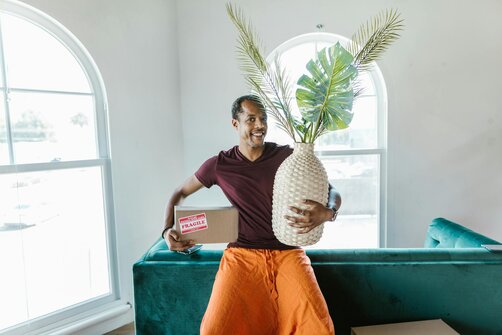 Man carrying decorative vase and box in bright room