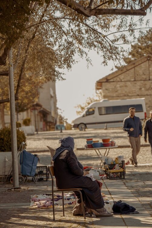 Veiled woman sitting outdoors at a sunny street market