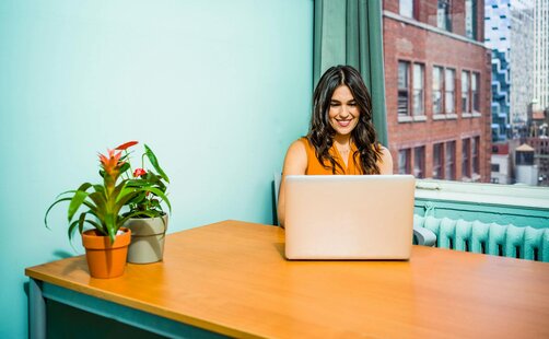 Smiling woman working on laptop at wooden desk
