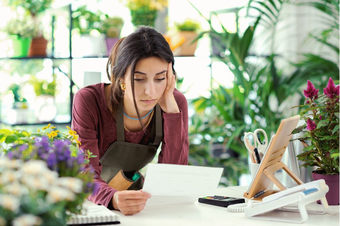 Worried woman reading document at flower shop counter desk