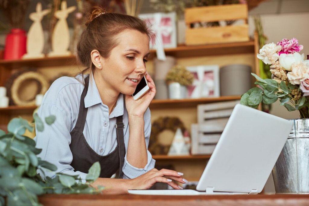 Florist talking on phone while using laptop at shop
