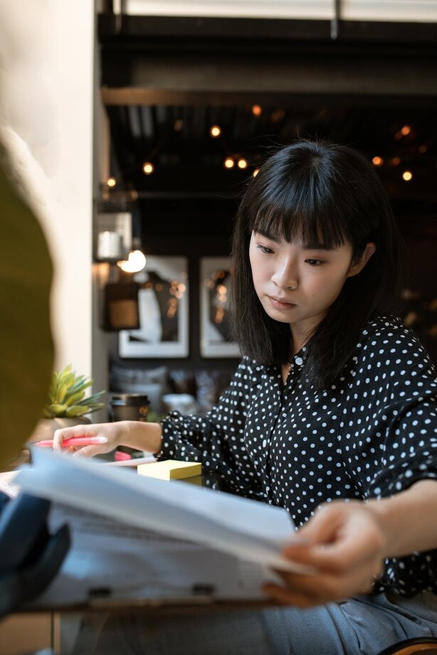Young woman carefully reading through printed documents at café