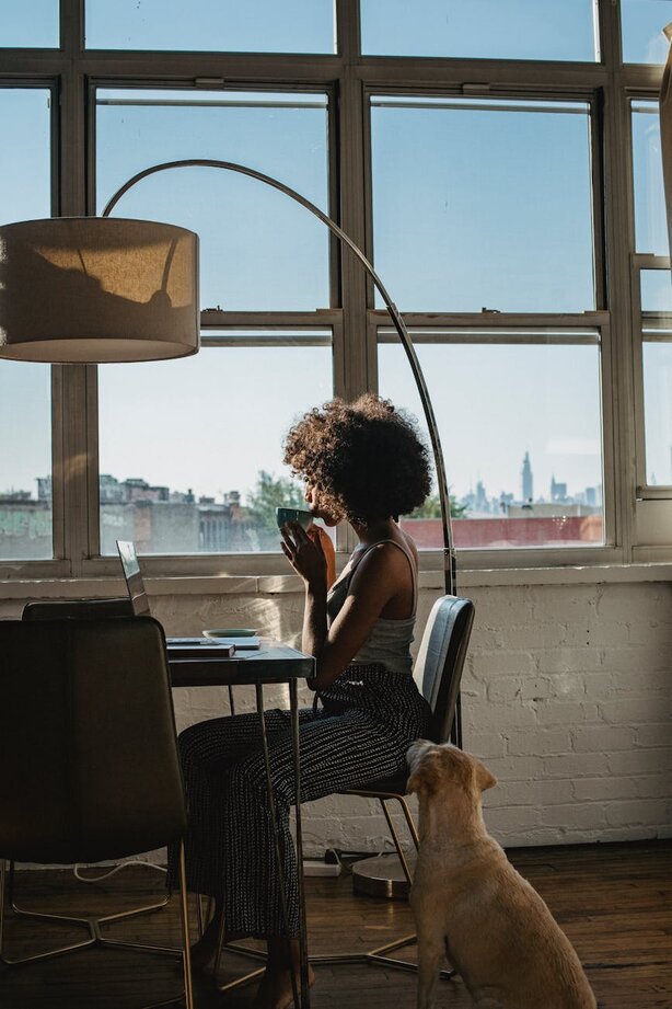 Woman sitting by window with dog and city view