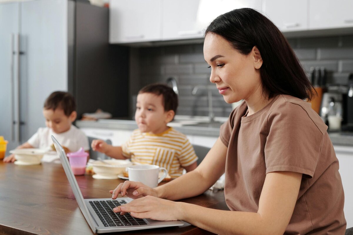 woman on her laptop while the kids are eating beside her