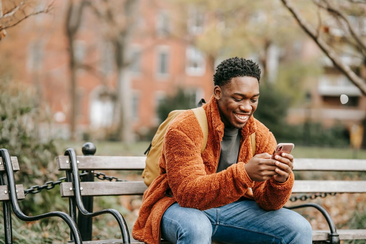 Happy young man using smartphone while sitting on park bench outdoors
