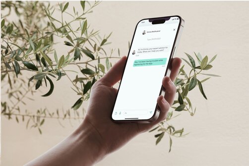Hand holding smartphone displaying app screen near green plants