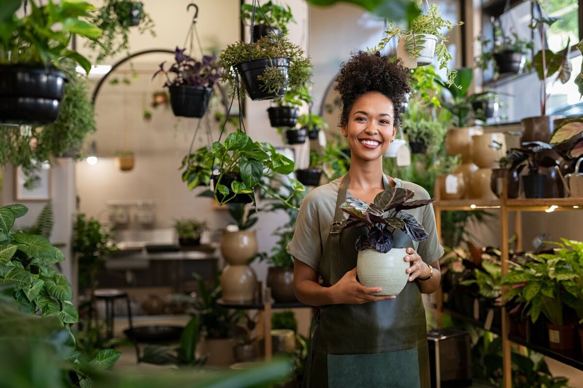 Smiling woman holding potted plant inside green plant shop