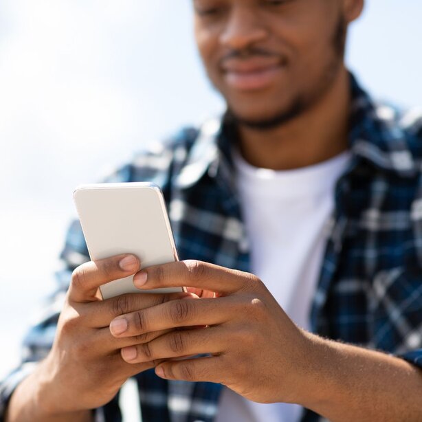 Young man in flannel shirt using smartphone outdoors
