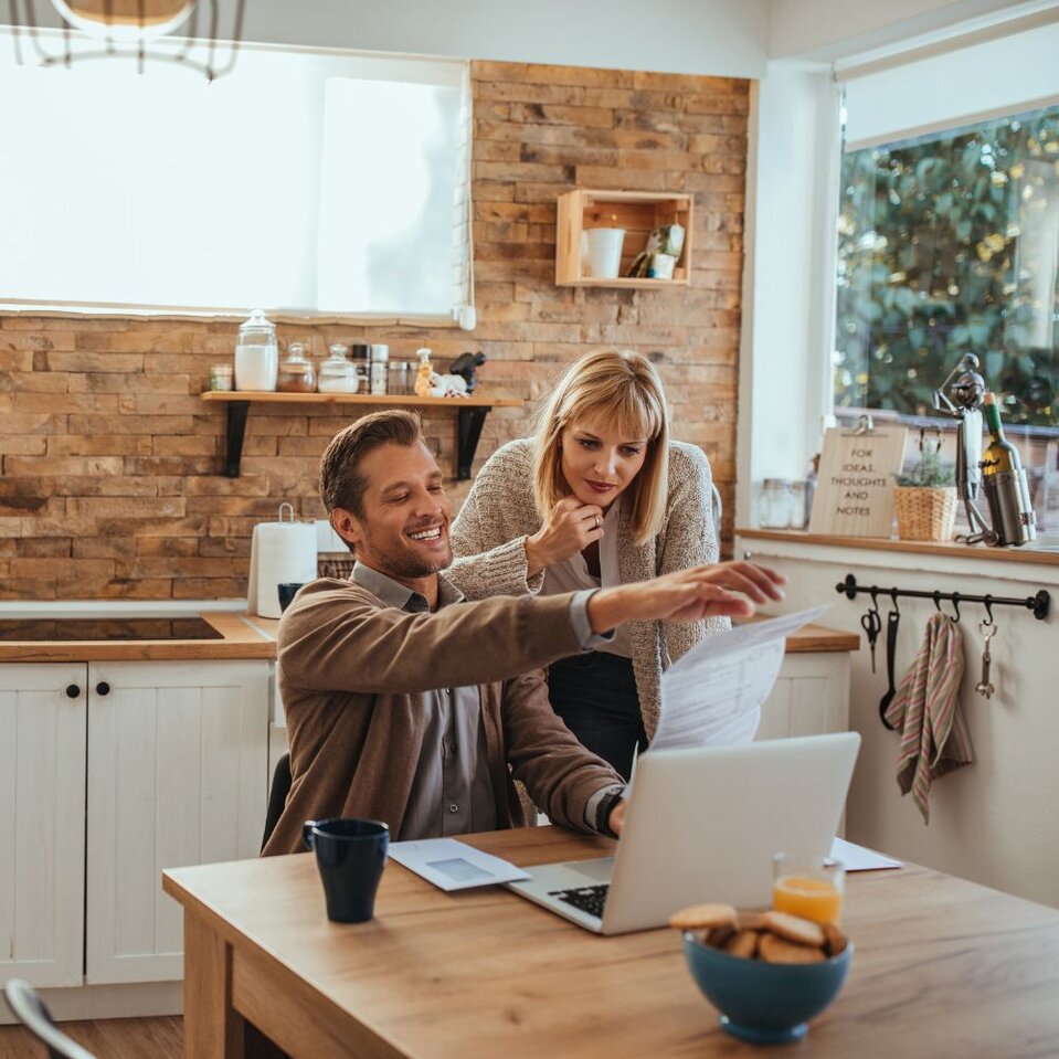 Couple smiling while reviewing documents together on home laptop