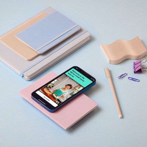 Smartphone displaying app screen placed among pastel stationery items