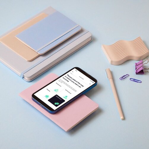Smartphone displaying app screen placed among pastel stationery items
