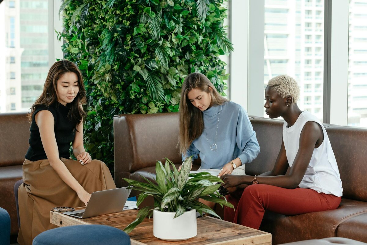three women sitting in a office on a brown sofa working 