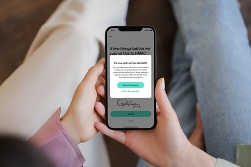 Hands holding a phone displaying a Pie Tax HMRC submission confirmation screen.