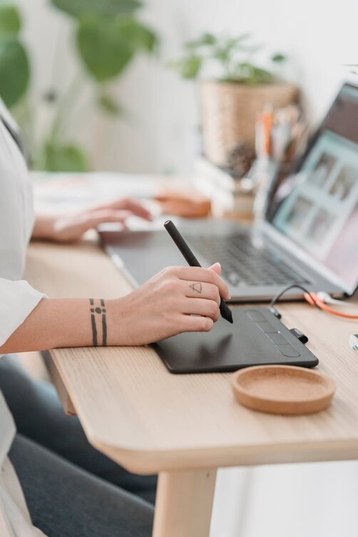 Designer using stylus on drawing tablet beside open laptop

