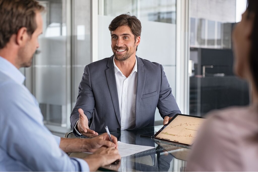Smiling businessman discussing documents with clients across office desk