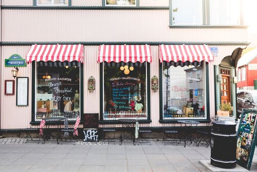 Storefront of a bistro with red-and-white striped awnings and outdoor seating on a sidewalk.