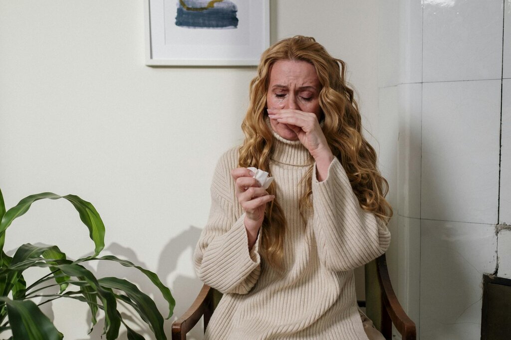 Distressed woman in cream sweater crying while holding tissue
