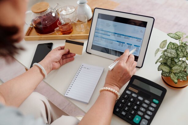 holding a card while using spreadsheet in a tablet and calculator and drinking tea