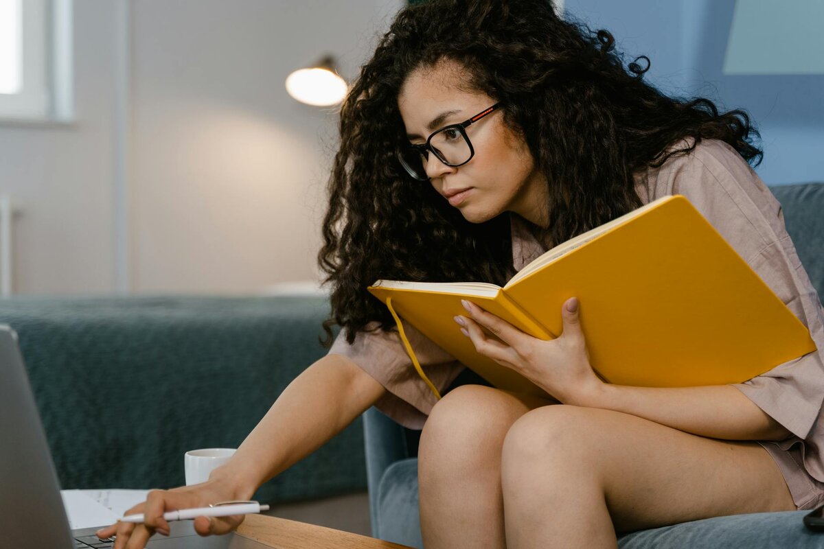 woman holding an orange notebook while browsing in her laptop