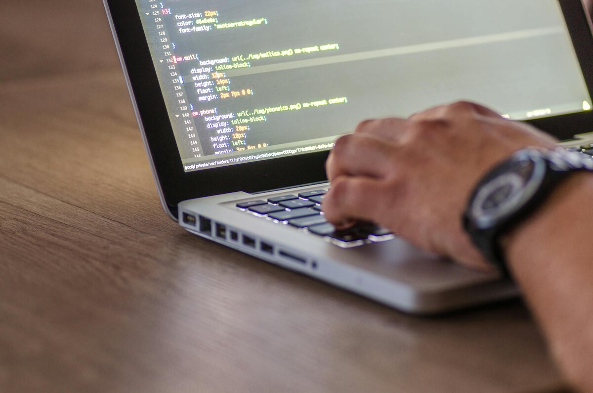 Close-up of a hand typing on a laptop displaying lines of code.