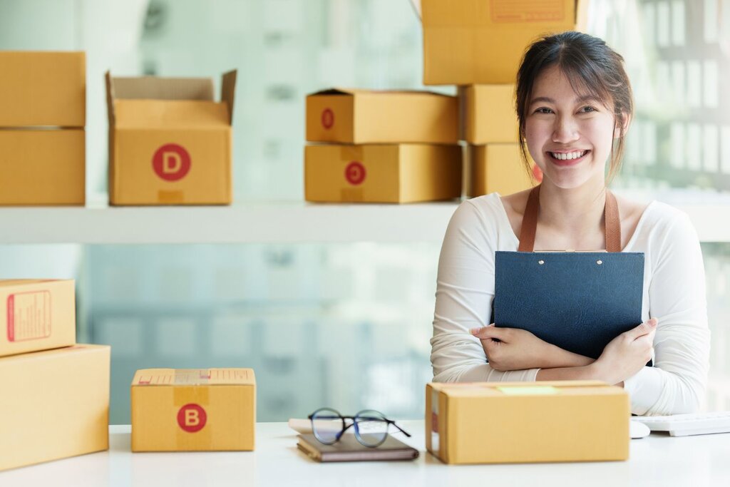 Smiling woman holding clipboard surrounded by labeled shipping boxes