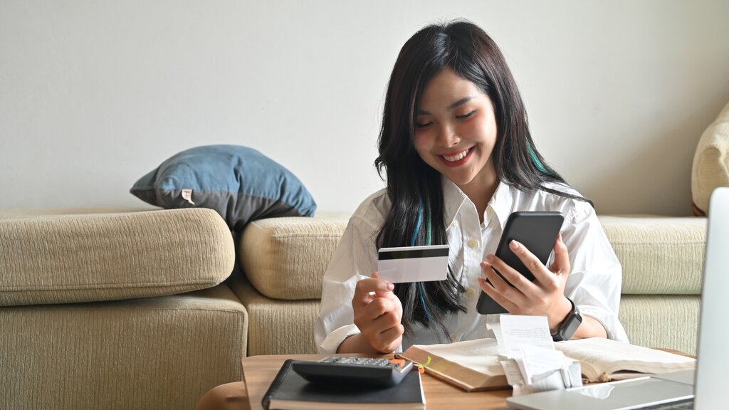 Woman holding card and phone with receipts nearby

