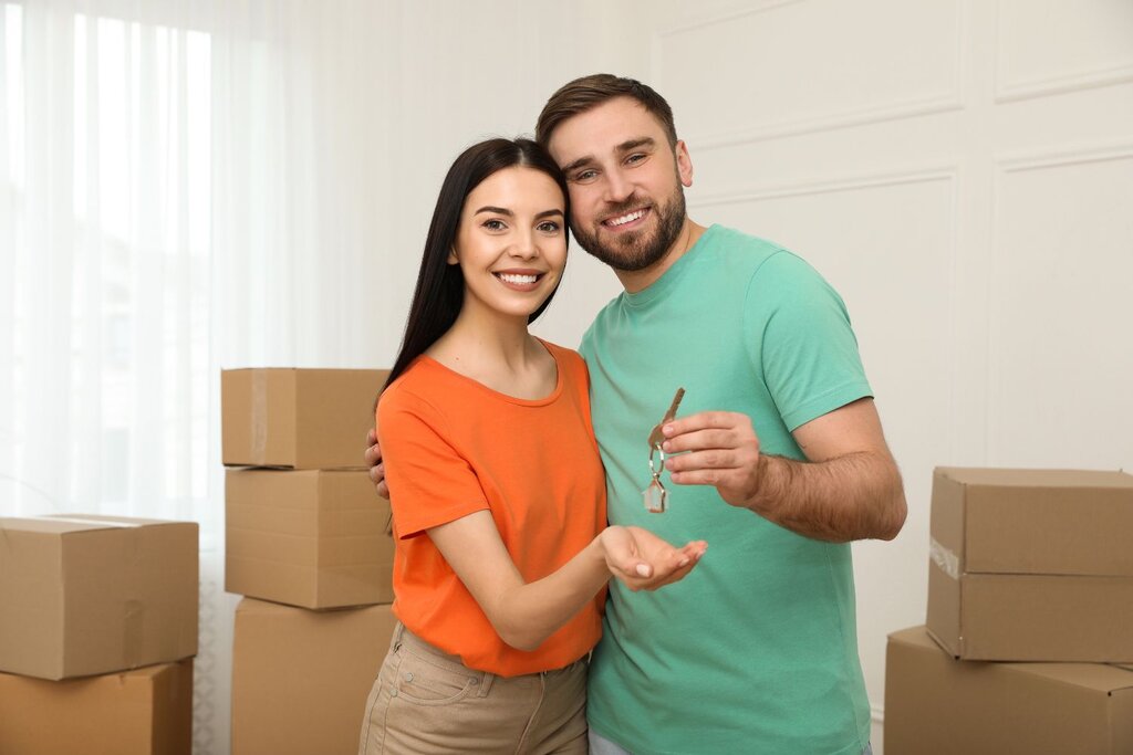 Happy couple holding keys surrounded by moving boxes