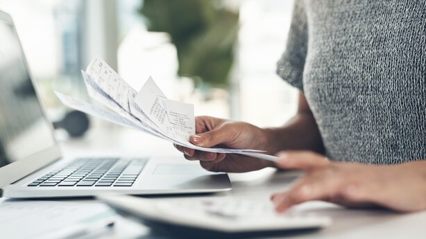 Hands sorting receipts beside laptop and calculator desk
