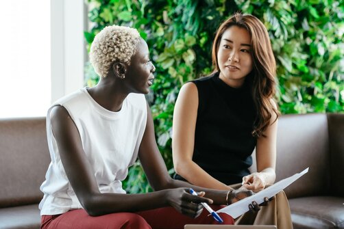 Two women smiling and conversing on couch with plants