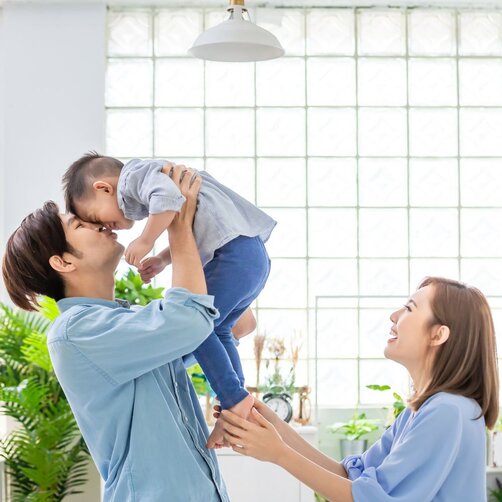 Father lifting baby while smiling mother watches at home