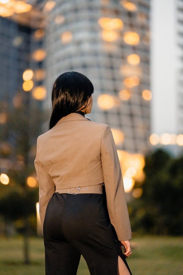 Woman in beige blazer standing before illuminated city building