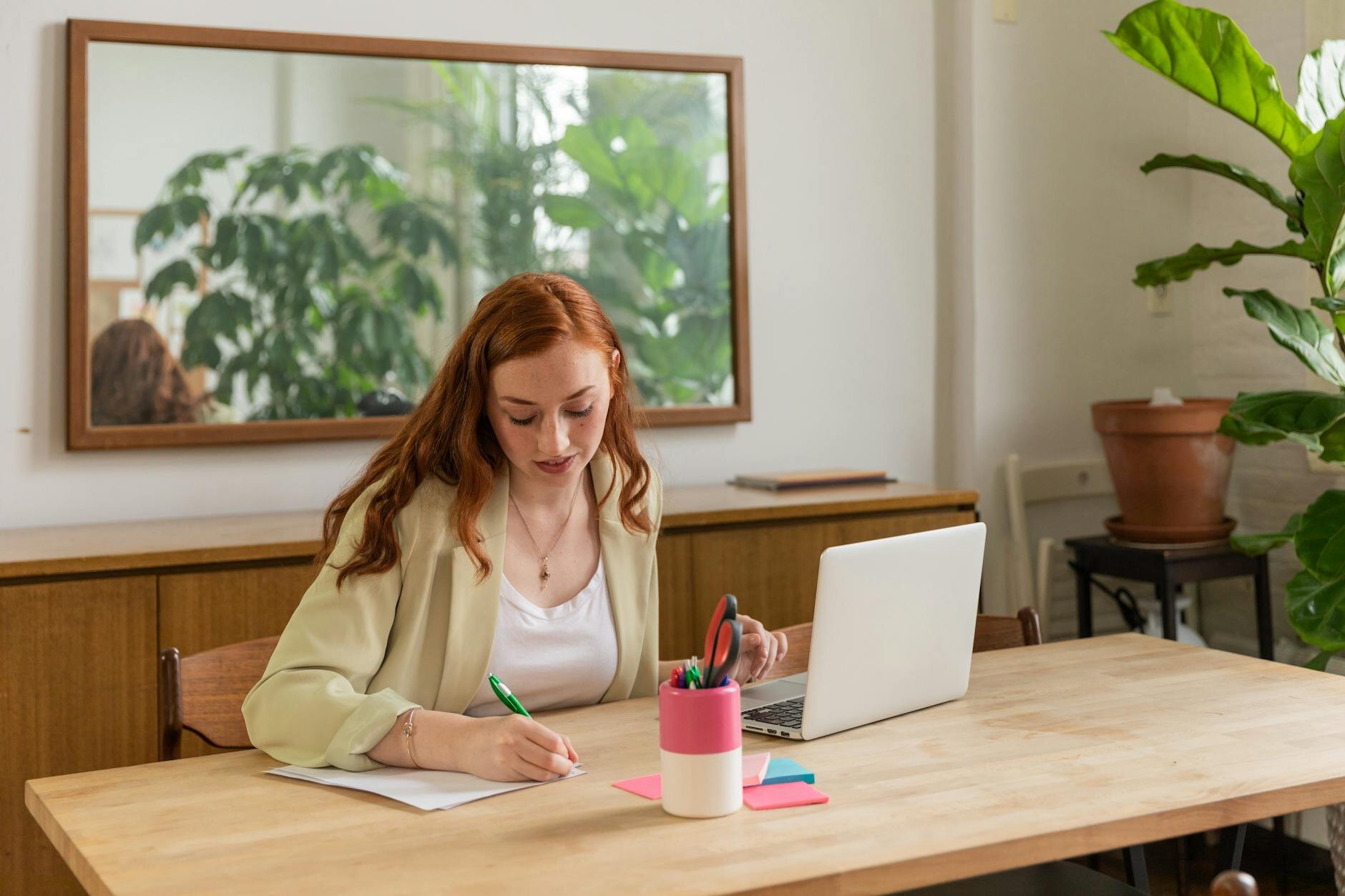 Woman writing notes at a desk with a laptop, working through her tax records"