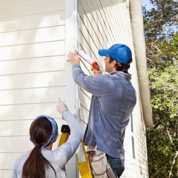 Two workers installing siding on exterior house wall