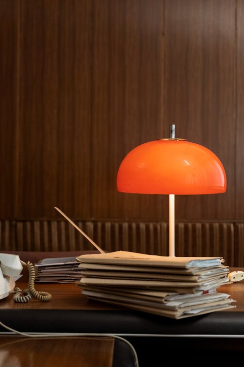 Retro orange mushroom lamp on desk with stacked magazines
