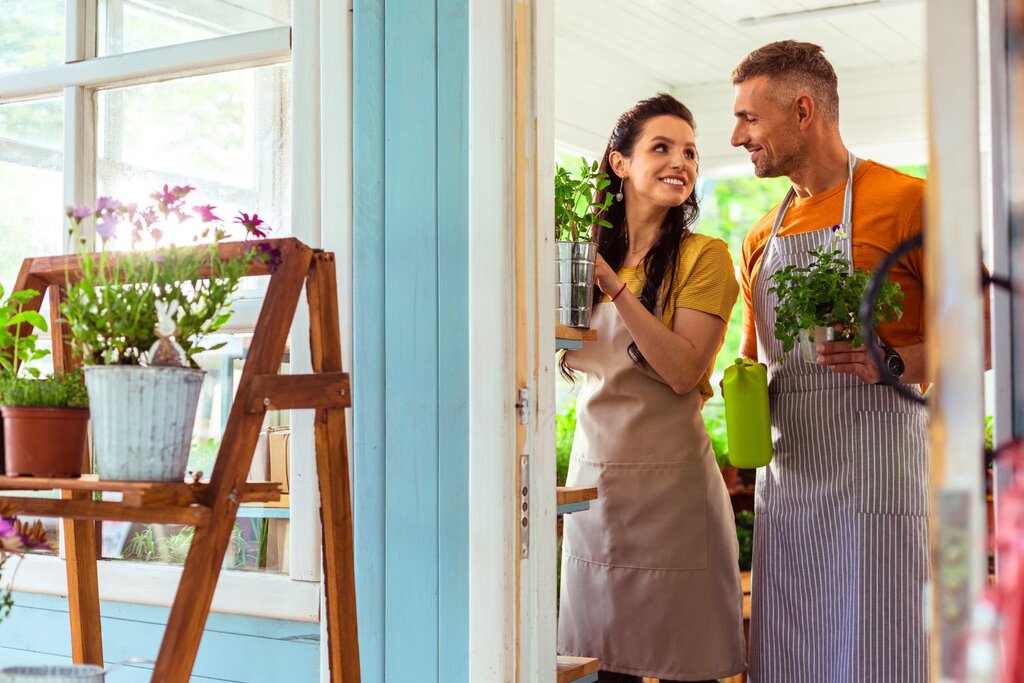 Two florist shop workers smiling together in doorway with plants