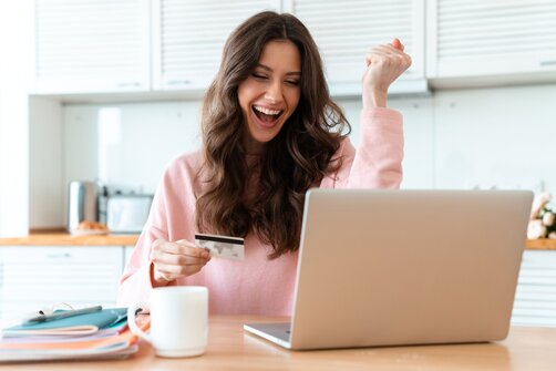 Excited woman holding credit card celebrating at home laptop