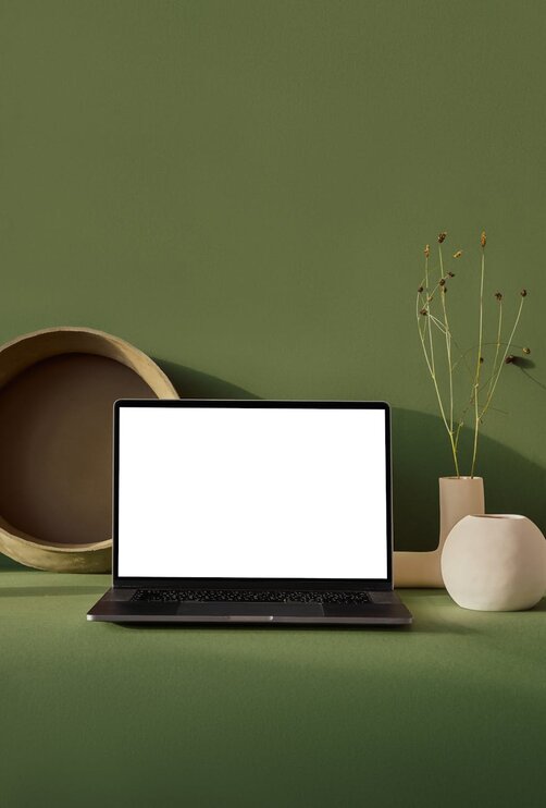 Laptop with blank screen on green desk with décor