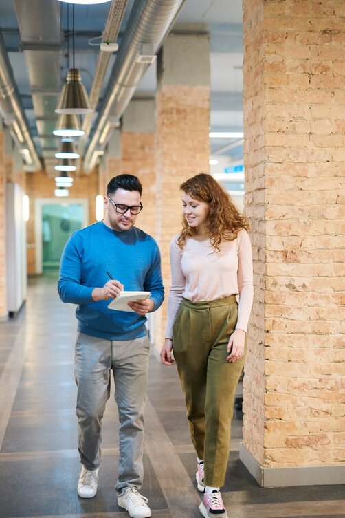 man and a woman walking down a hallway looking at a piece of paper