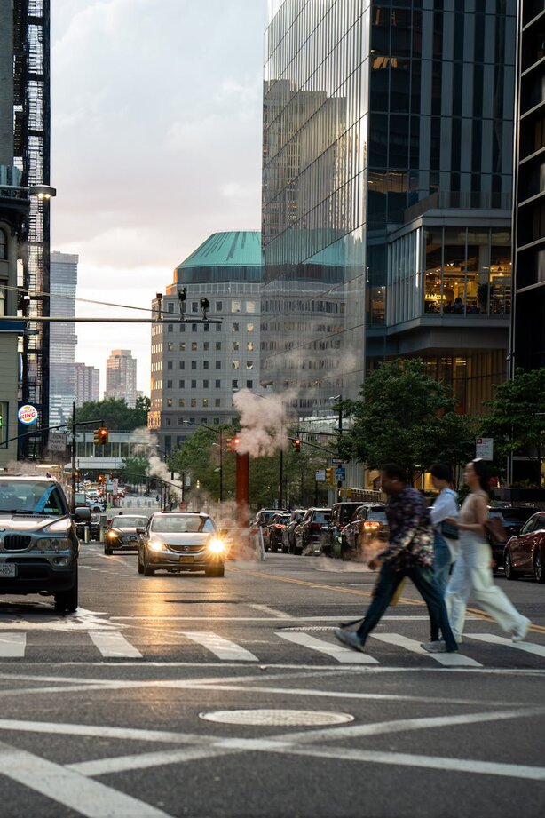 Pedestrians crossing busy city street at dusk with steam