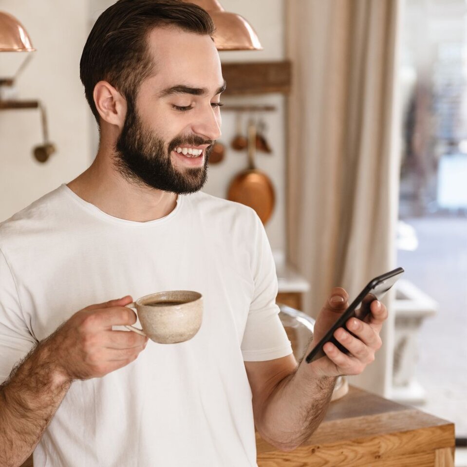 Man enjoying coffee while checking phone in kitchen