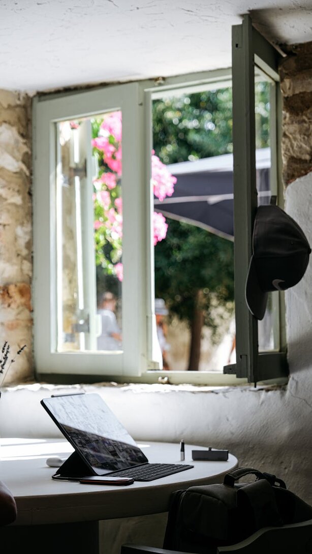 Laptop on desk beside open window with flower view