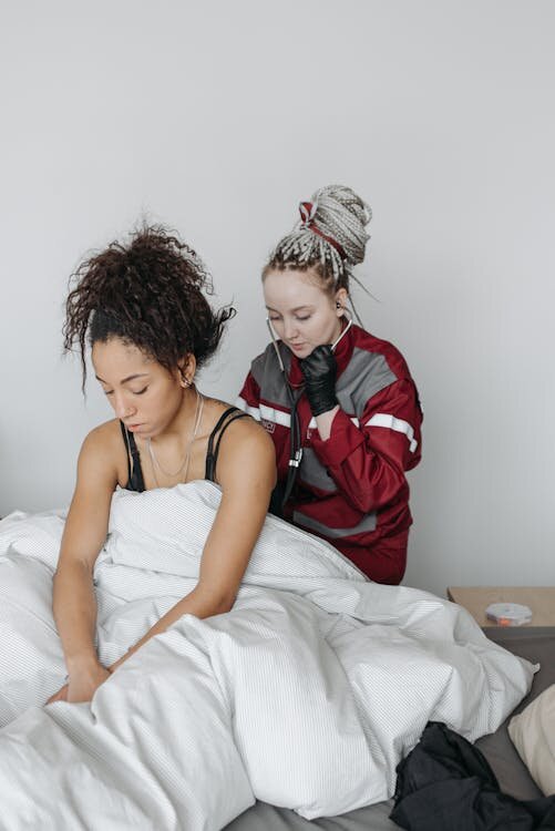 Two young women sitting together on bed looking downward