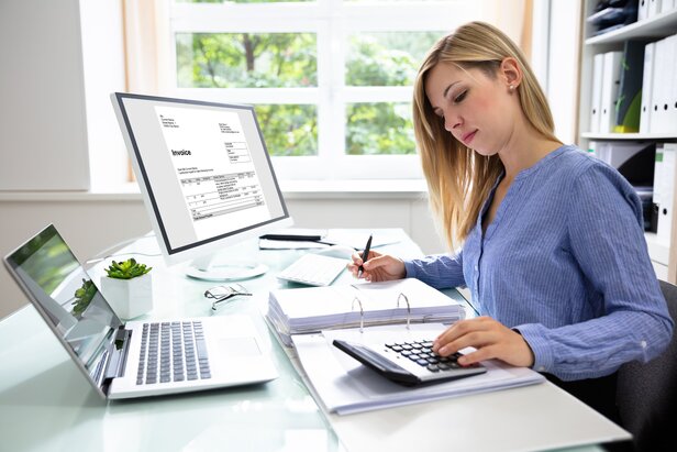 Woman using calculator and laptop for accounting at desk