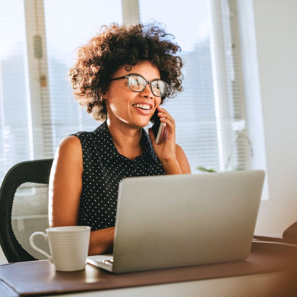 Woman smiling during phone call while using laptop